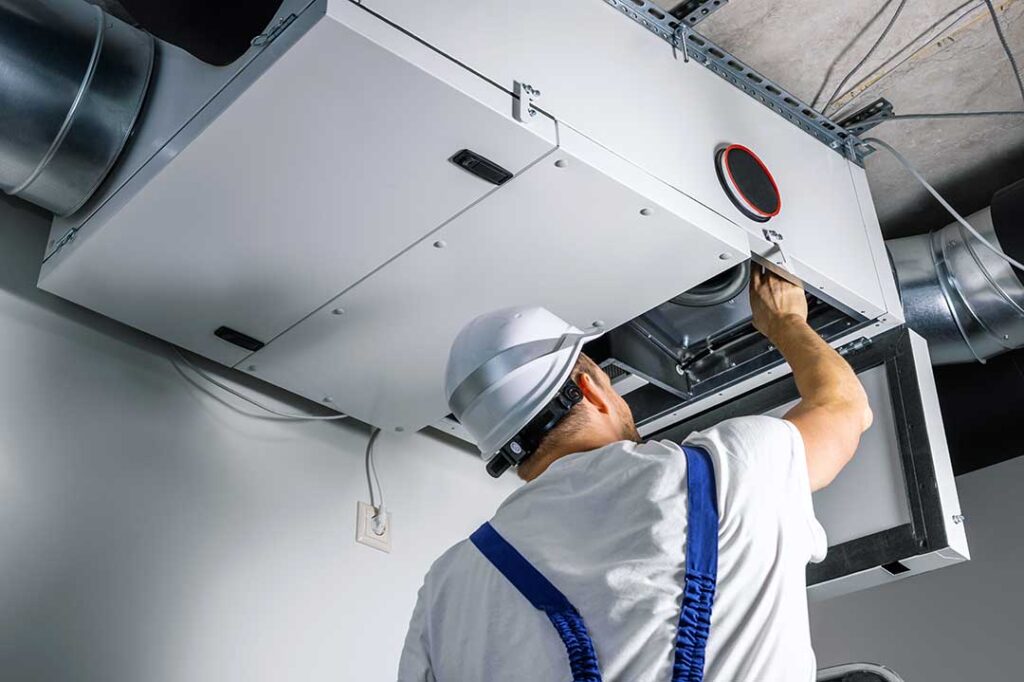 A homeowner slides a pleated air filter into the return-air compartment beside a basement furnace.