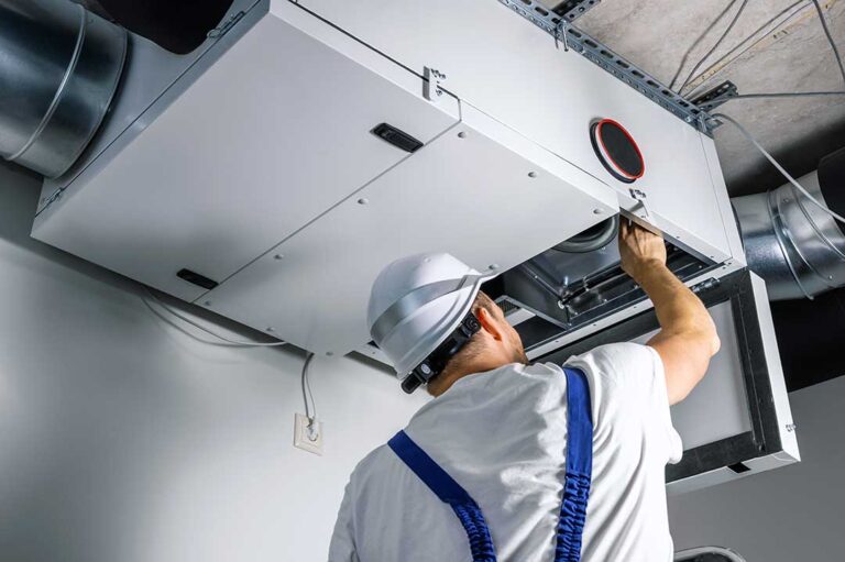 A homeowner slides a pleated air filter into the return-air compartment beside a basement furnace.