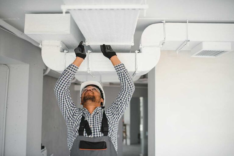Technician inspecting a residential furnace beside ductwork with tools and a flashlight.